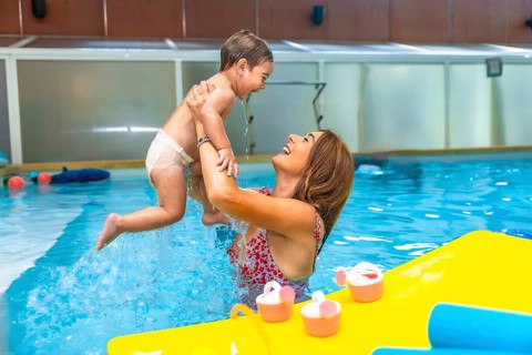 Happy mother lifting her laughing baby out of the water in an indoor swimming pool next to floating