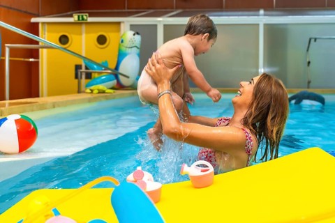 Smiling mother lifting her baby while playing in a swimming pool during a sunny day, enjoying their