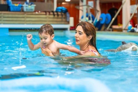 Swimming instructor holding baby swimming in indoor pool during a lesson, promoting water safety