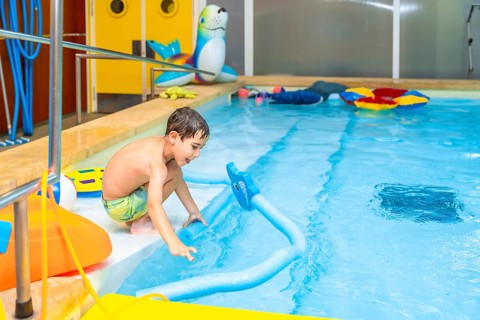 Boy enjoying playful moments with a colorful pool noodle float in an indoor swimming pool,