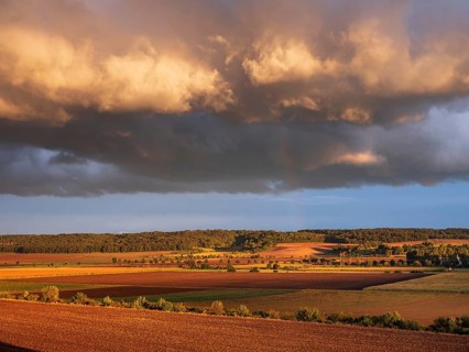 Field landscape in autumn, ploughed fields under dark storm clouds with rainbow in the evening
