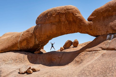Tourist jumping in a rock arch, round rock formations with stone arch, Pontok Mountains, Great