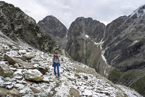 Mountaineer on steep rocky mountain landscape with fresh snow in summer, behind mountain peaks