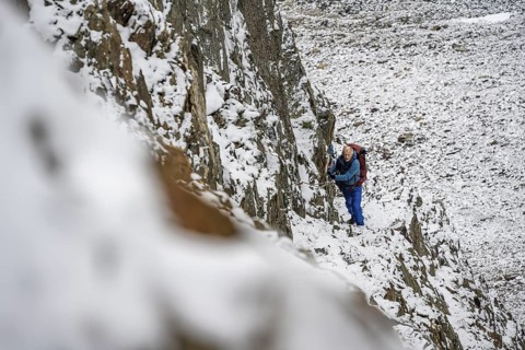 Mountaineer on a rope-secured path in a steep, rocky mountain landscape with fresh snow in summer,
