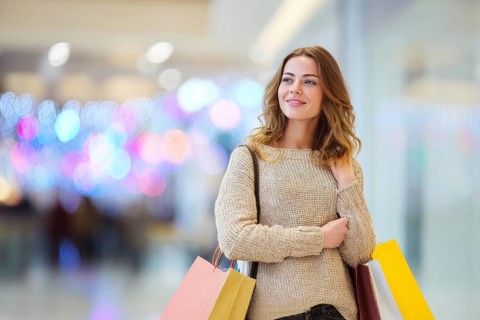 Beautiful young happy attractive woman with bags of different colours in shopping center mall