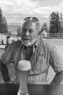 Elderly gentleman with beard and sunglasses in a garden restaurant with a drink, black and white,