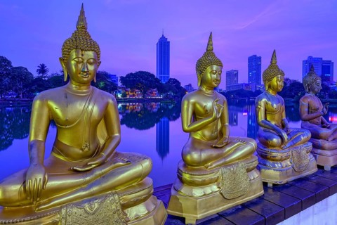 Buddha statues of Seema Malaka Temple at Beira Lake at sunset, Colombo skyline behind, Sri Lanka