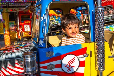 Young boy with a joyful expression sitting in a colorful amusement park ride, surrounded by bright