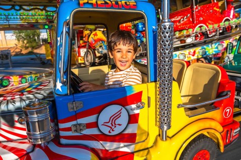 Smiling child enjoying a vibrant amusement park ride, sitting in a brightly colored truck,