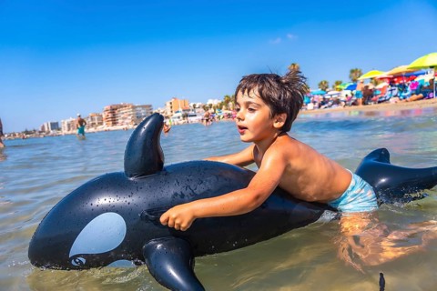 Happy child riding on an inflatable orca toy in the sea, splashing through waves and enjoying a