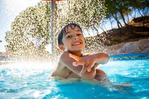 Smiling boy enjoying playful moments under a refreshing water shower in a swimming pool on a
