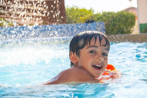 Smiling child enjoying summer vacations playing in a blue swimming pool with inflatable armbands