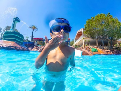 Young boy wearing sunglasses blowing a kiss while standing in a swimming pool at a water park with