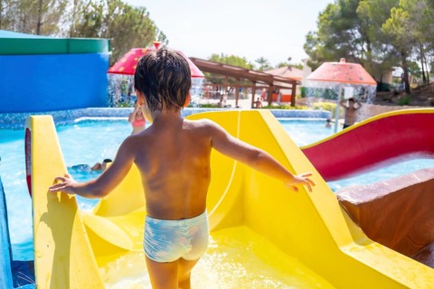 Young boy climbing up a vibrant yellow waterslide at a lively water park, embracing the joy of