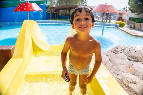 Smiling boy holding a toy car, enjoying summer vacation while sliding down a bright yellow