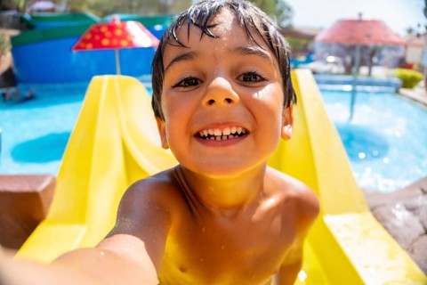 Smiling boy taking a selfie while having fun on a waterslide at a water park during summer vacation