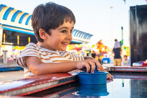 Smiling young boy playing a game at an amusement park, surrounded by colorful attractions and