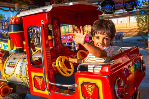 Smiling child enjoying a ride on a vibrant amusement park train, waving enthusiastically. Bright