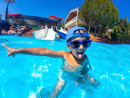 Playful child with blue sunglasses and hat pointing with finger and sticking tongue out in a