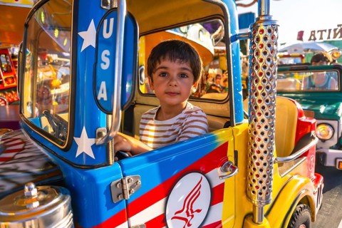 Young boy driving a vibrant, colorful toy truck while enjoying a playful day at a funfair carousel,