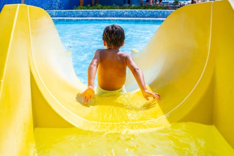 Boy joyfully sliding down a colorful waterslide in an aquapark, enjoying summer vacation with