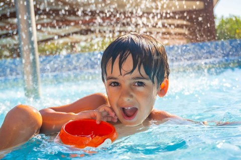 Portrait of a smiling child playing with an orange plastic bucket in a swimming pool under water