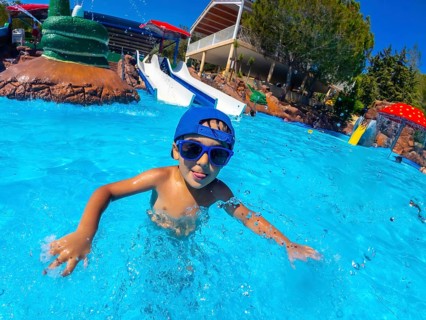 Young boy wearing sunglasses and a blue cap, enjoying a summer day at a water park, swimming in the