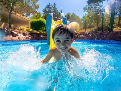 Young boy enjoying a sunny day, sliding into a vibrant blue pool with a big splash, surrounded by