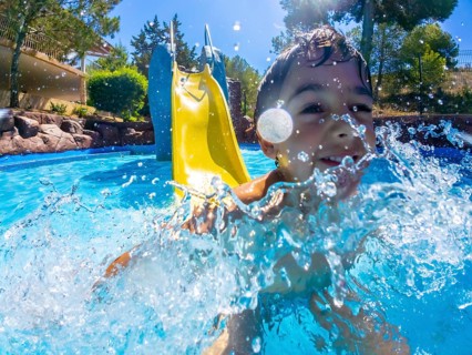 Young boy having fun going down a water slide and splashing into a refreshing pool on a sunny