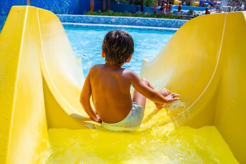 Young boy enjoying summer holidays sliding down yellow waterslide into swimming pool in aqua park