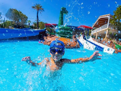 Happy child wearing blue baseball cap and swimming goggles, playing and splashing in a pool during