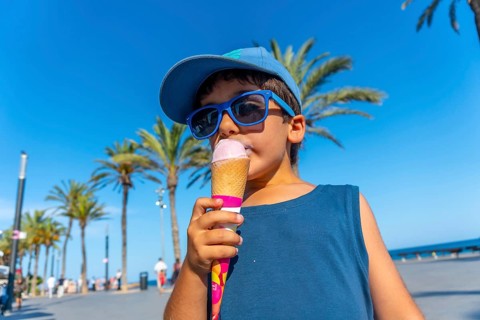 Young boy wearing sunglasses and cap enjoying a refreshing ice cream cone on a sunny summer day at