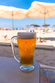 Ice cold beer sitting on a beach bar counter, with white beach umbrellas and ocean in the