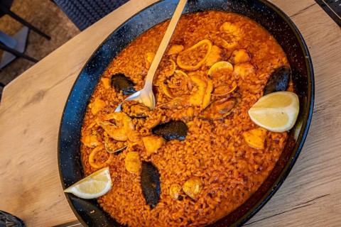 Large pan of delicious seafood paella with shrimps, mussels, squid, clams, and lemon wedges, ready