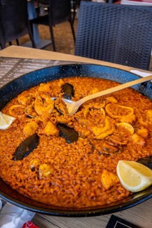 Steaming paella with mussels, shrimp, and calamari, served in a traditional pan and garnished with