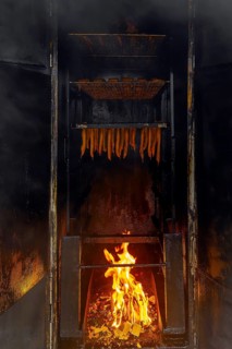 Smoking fish over beechwood fire in large metal smoker oven on the island Usedom in the Baltic Sea,
