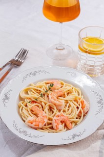 Pasta with shrimp and thyme, served on a white plate, with a glass of white wine, the table is set,