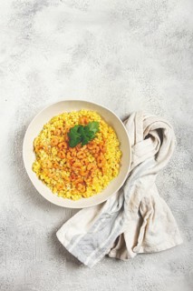 Risotto with shrimp, in a bowl, on a textured surface, with a side dish of fresh coriander,