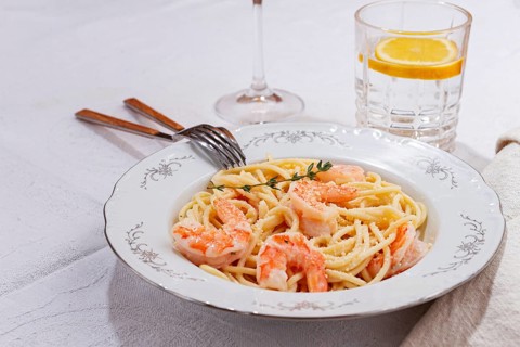 Pasta with shrimp and thyme, served on a white plate, with a glass of white wine, the table is set,