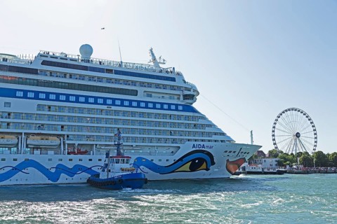 Cruise ship AIDA nova is pressed against quay wall by tugboat, Ferris wheel, Warnow, Warnemünde,