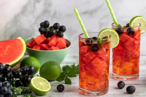 Two glasses of watermelon, grape and lime drink surrounded by ingredients