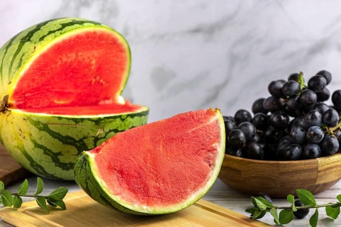 Sliced watermelon and grapes on a wooden board with mint leaves