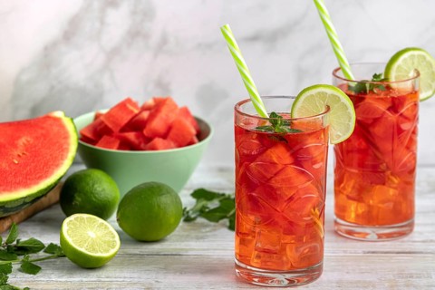 Two glasses with watermelon and lime drink surrounded by ingredients