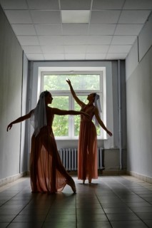 Silhouette of two dancers performing graceful artistic moves with their hands in corridor of