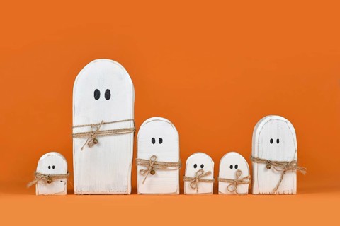 Cute wooden white Halloween ghost ornaments in a row on orange background