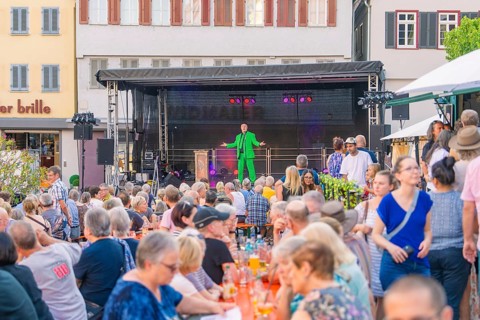 A man on stage entertains a large audience at an outdoor event, 950 years Weil der Stadt ceremony,