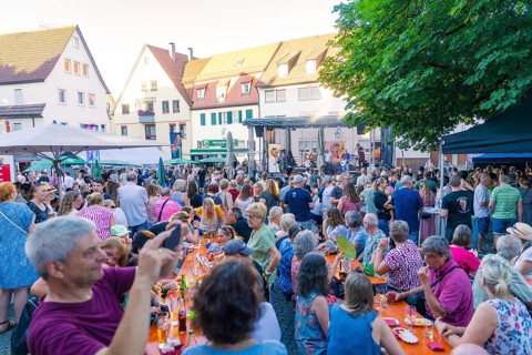 Large crowd enjoying an outdoor concert with seats and surrounding houses, 950 years Weil der Stadt