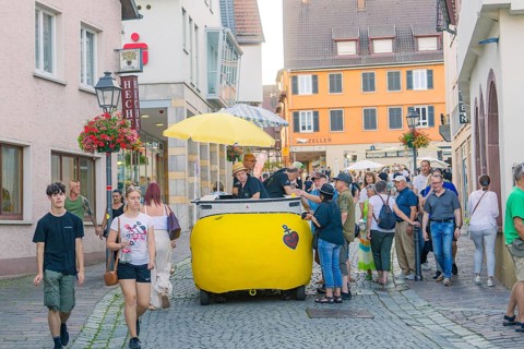 People stroll through a narrow alley in the old town centre, flanked by shops and flowers, 950th
