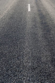 Rustige asfaltweg zonder voertuigen, met een enkele witte middenlijn zichtbaar. De weg strekt zich