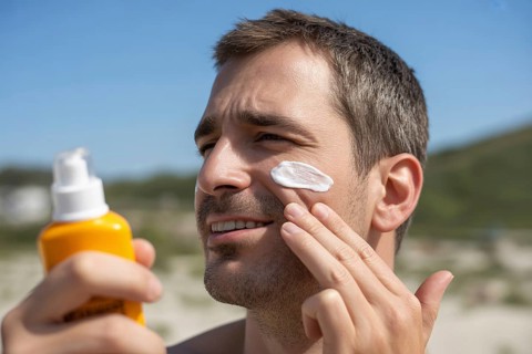 Man applying sunscreen to his cheek on a sunny summer day with beach in background. Generative Ai,